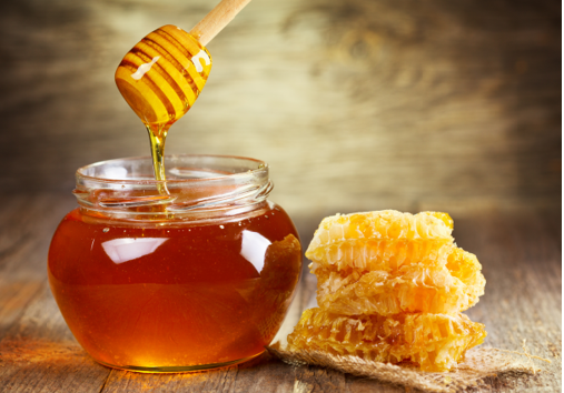 Raw honey in a glass jar with wooden dipper