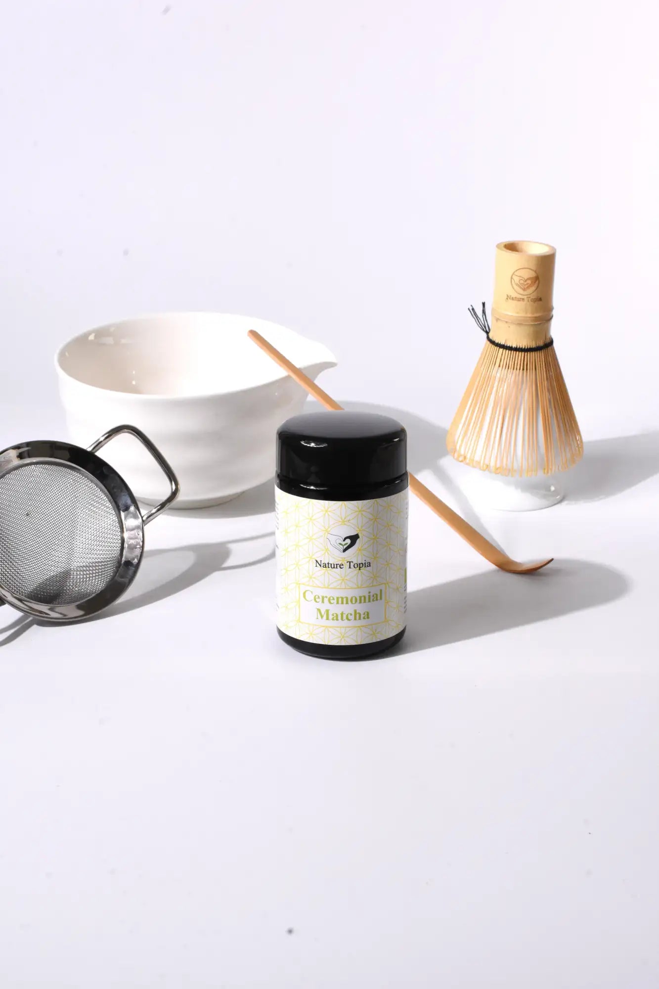 Grüntee-Dose mit weißem Etikett und schwarzem Deckel, Keramikschüssel, Bambusbesen.